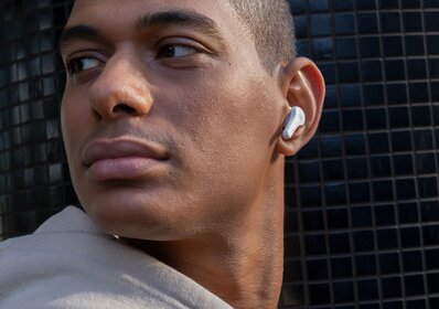 Mann med Urban Vitamin trådløse ørepropper i øret, poserer foran en moderne bygning med svart flislagt vegg.