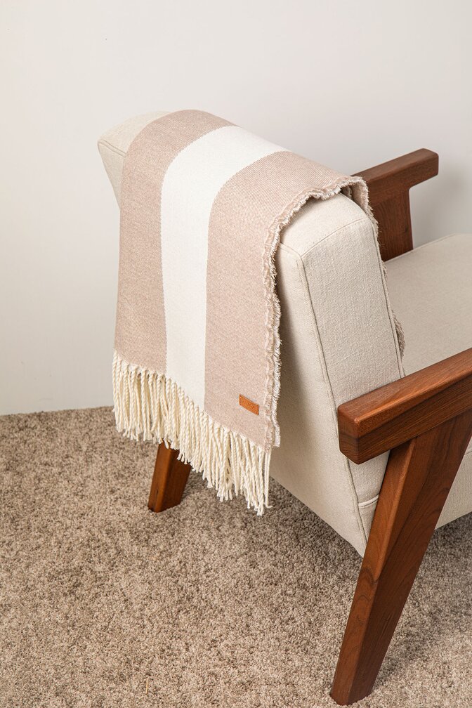 Myk og elegant ullpledd med frynser drapert over en moderne lenestol – en perfekt påskegave for hygge og hjemmekos.