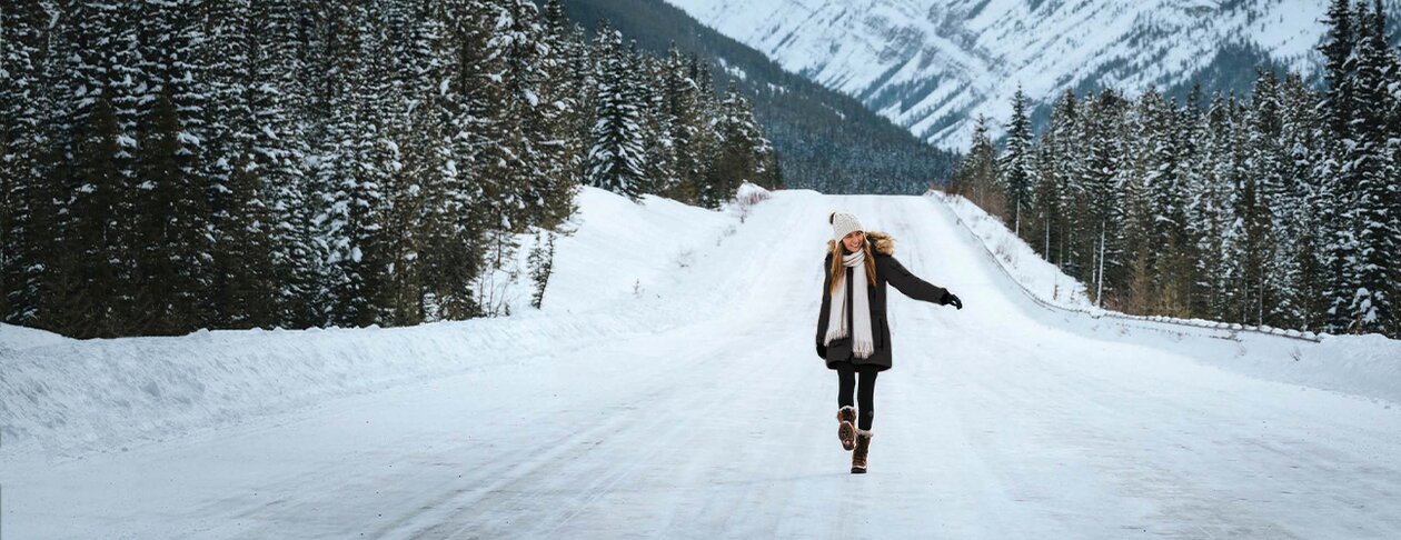Kvinne iført Stormtech vinterjakke og skjerf går på en snødekt vei med fjell i bakgrunnen