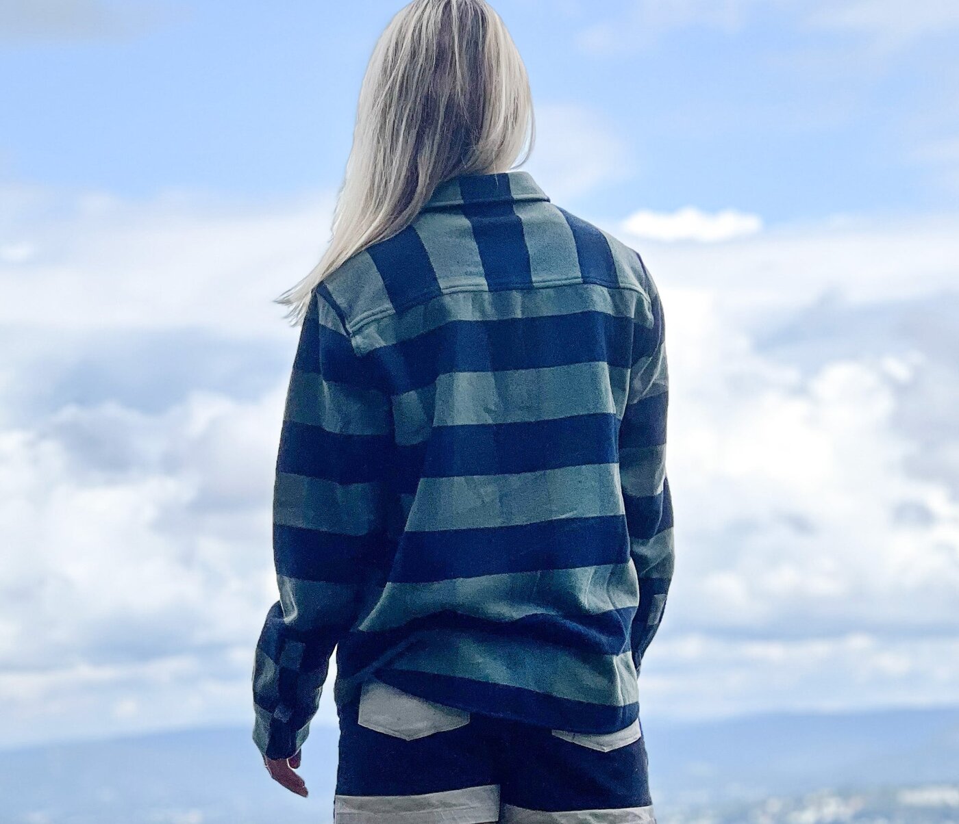 Kvinne i Tufte-overshirt står på et fjell og ser utover dalen, med skyer over åsene.