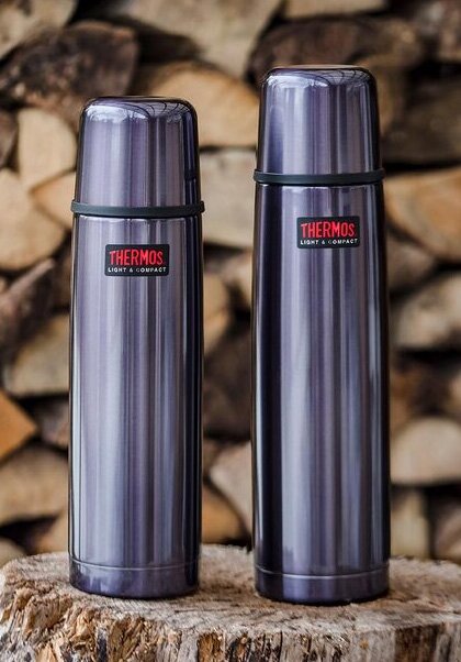 To stålfargede Thermos ‘Light & Compact’-termoser foran en vedstabel.