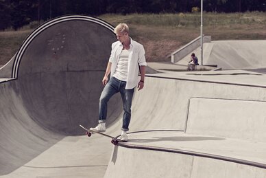 Mann på skateboard i skatepark, iført hvit skjorte og jeans fra Printer.