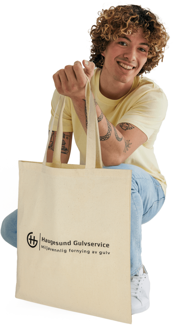 Mann i lys T-skjorte som sitter på huk med et naturfarget handlenett merket Haugesund Gulvservice.