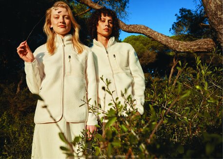 To kvinner i hvite Iqoniq-fleecejakker står i en skog.