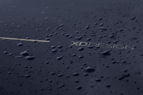 Nærbilde av en svart XD Design-ryggsekk med vanndråper på overflaten, som viser vannavstøtende materiale.