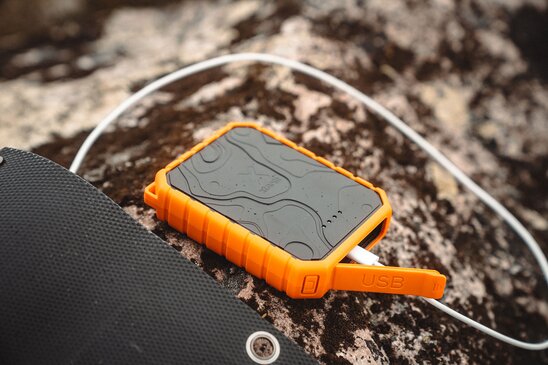 Oransje Xtorm-powerbank med USB-kabel tilkoblet, liggende på en stein.
