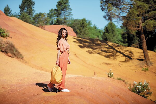 Kvinne i oransje antrekk bærer en matchende XD Design-ryggsekk i et fargerikt, ørkenlignende landskap.