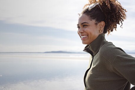 Smilende kvinne i grønn Cutter & Buck-jakke ved kysten.