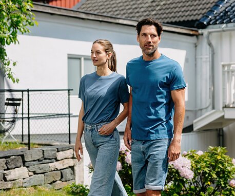 Mann og kvinne i blå t-skjorter fra YOU® kolleksjonen, utendørs i en hage