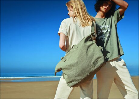 En kvinne og en mann på en strand iført Iqoniq-T-skjorter, med en stor grønn veske.