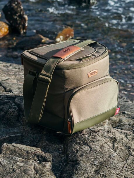 Grønn Thermos-kjølebag i robust stoff, plassert på en stein ved sjøen.