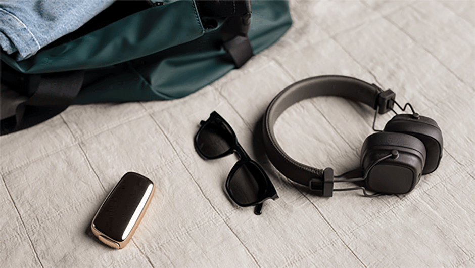 Ploom device, black sunglasses, and wireless headphones next to an open backpack on the bed.