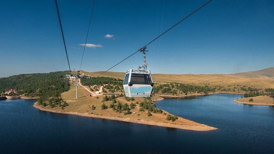 Cable car over calm lake, green hills and blue sky, blending peace and adventure.