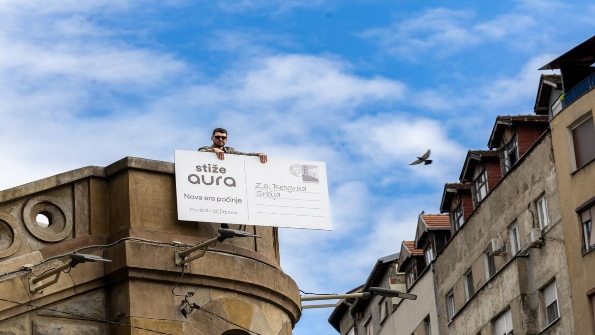 Person on a ledge with a postcard, bird flying, city below, bright blue sky, adventurous mood.