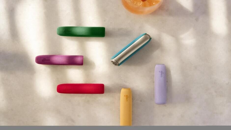 Ploom AURA device on a light marble surface surrounded by back covers in all colors.