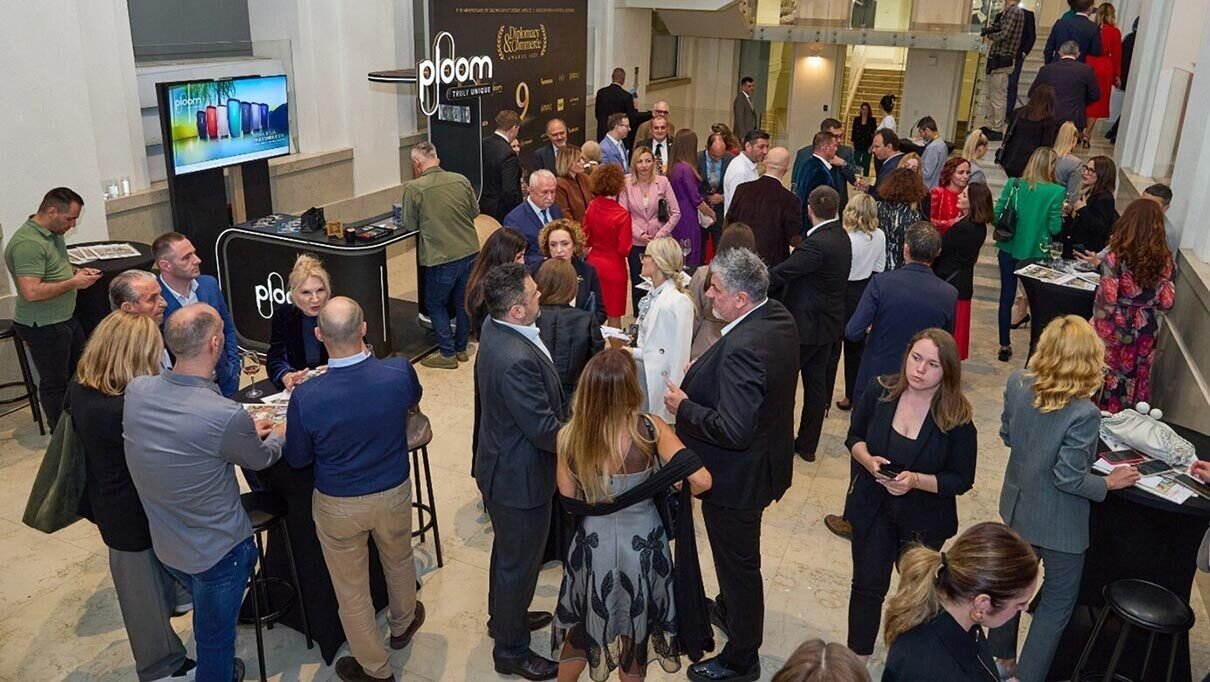 Okupljanje ljudi oko štanda brenda 'Ploom' sa sloganom 'Truly Unique' u konferencijskoj sali.