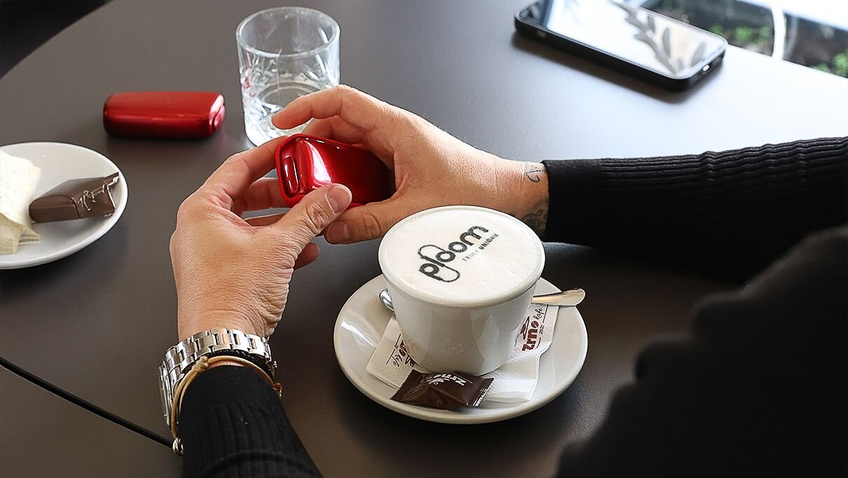 A man is drinking Ploom coffee and holding his Ploom X Advanced Red.