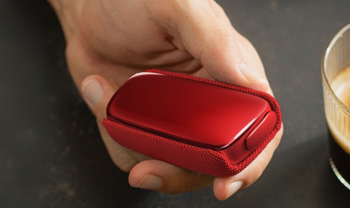 Covek sedi u kaficu, pije Ploom kafu i drzi svoj Ploom X Advanced Red