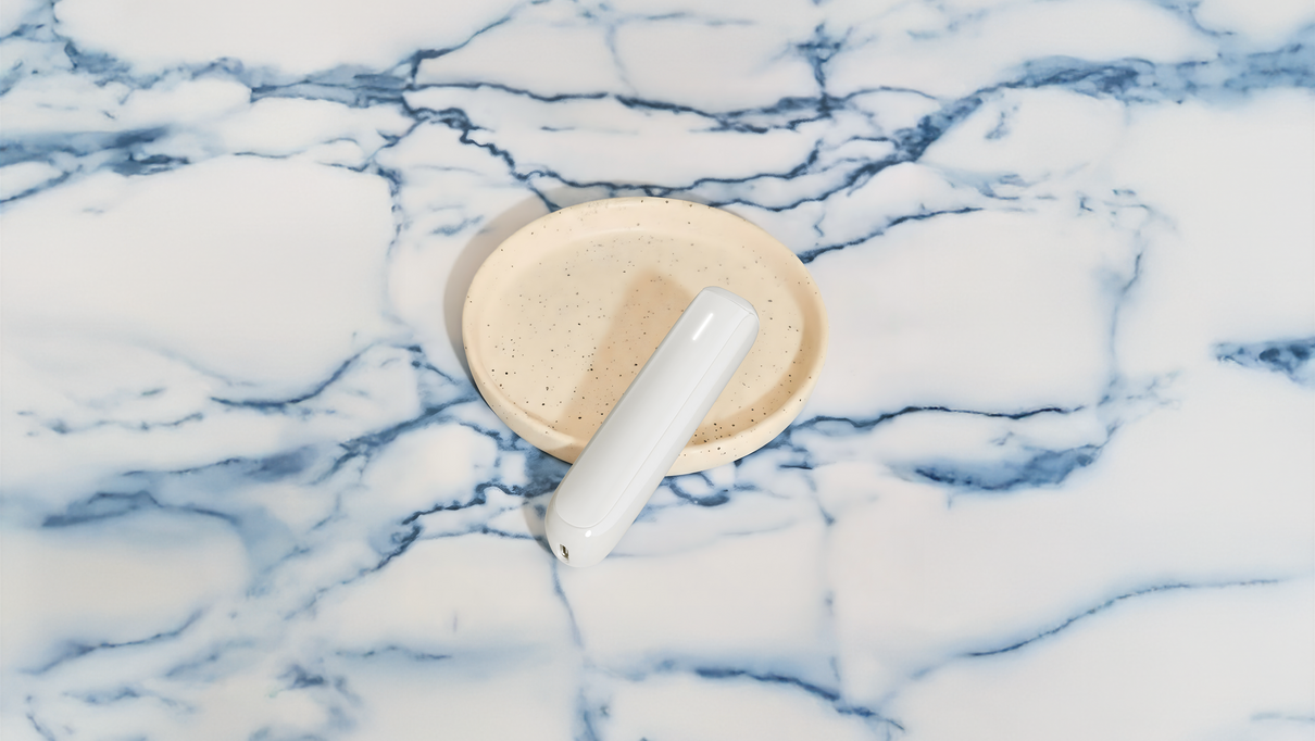 Ploom AURA Glacier White device leaning against a case, placed on a marble table that gives off blue-white tones.