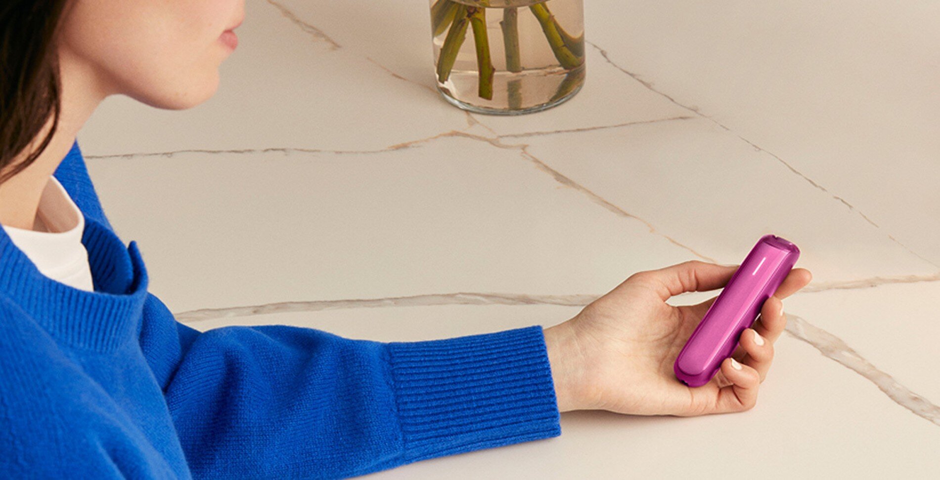 Devojka drži Ploom AURA Fushia Flair uređaj u ruci na svijetloj površini