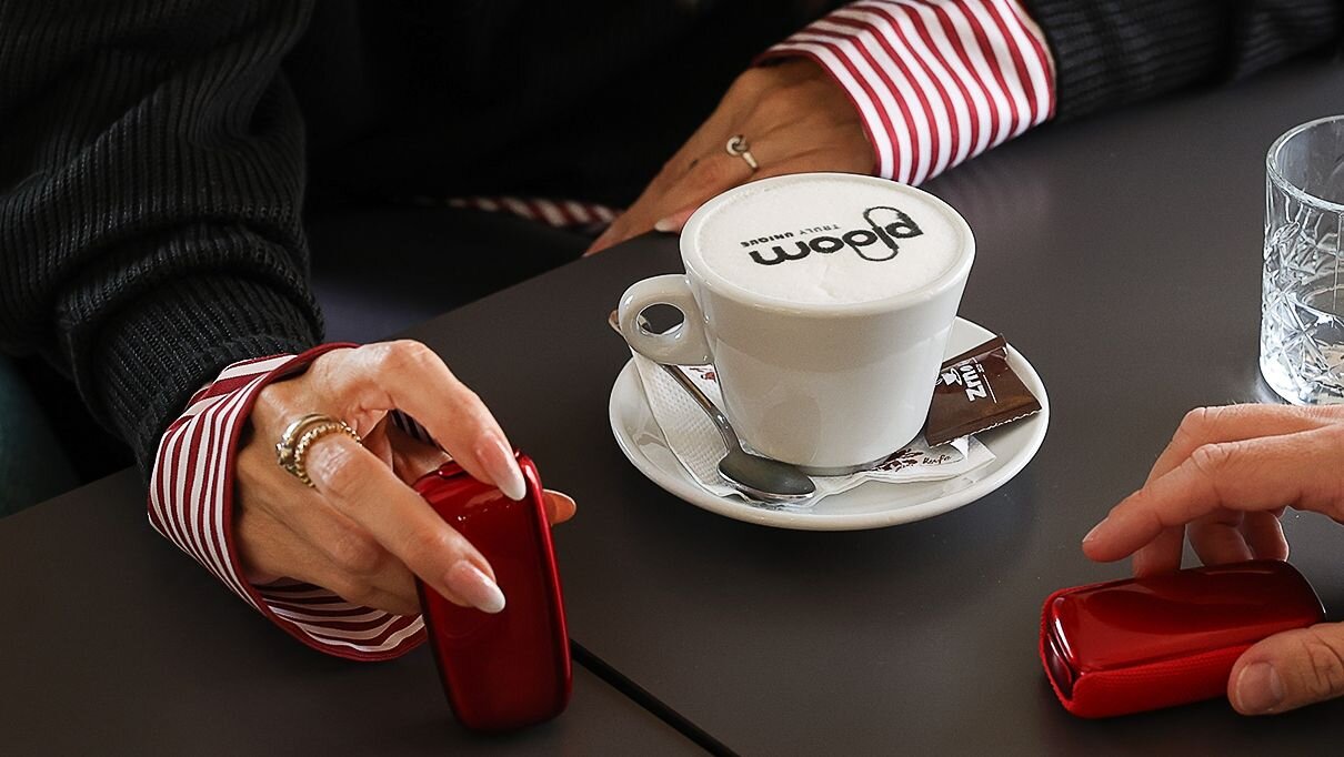 Woman is drinking Ploom coffee and holding the Ploom X Advanced Red.