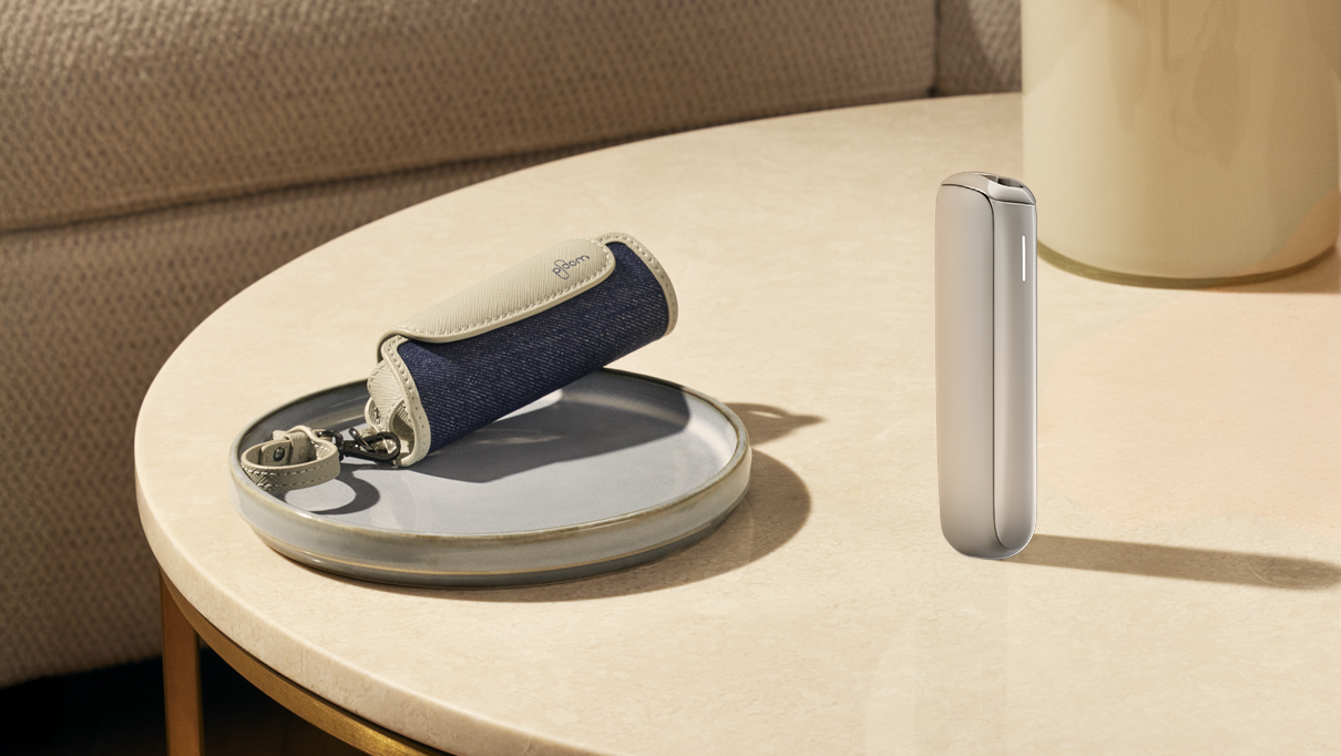 The Ploom AURA Lunar Silver stands upright on a table, next to a round tray with a Solo Denim pouch.