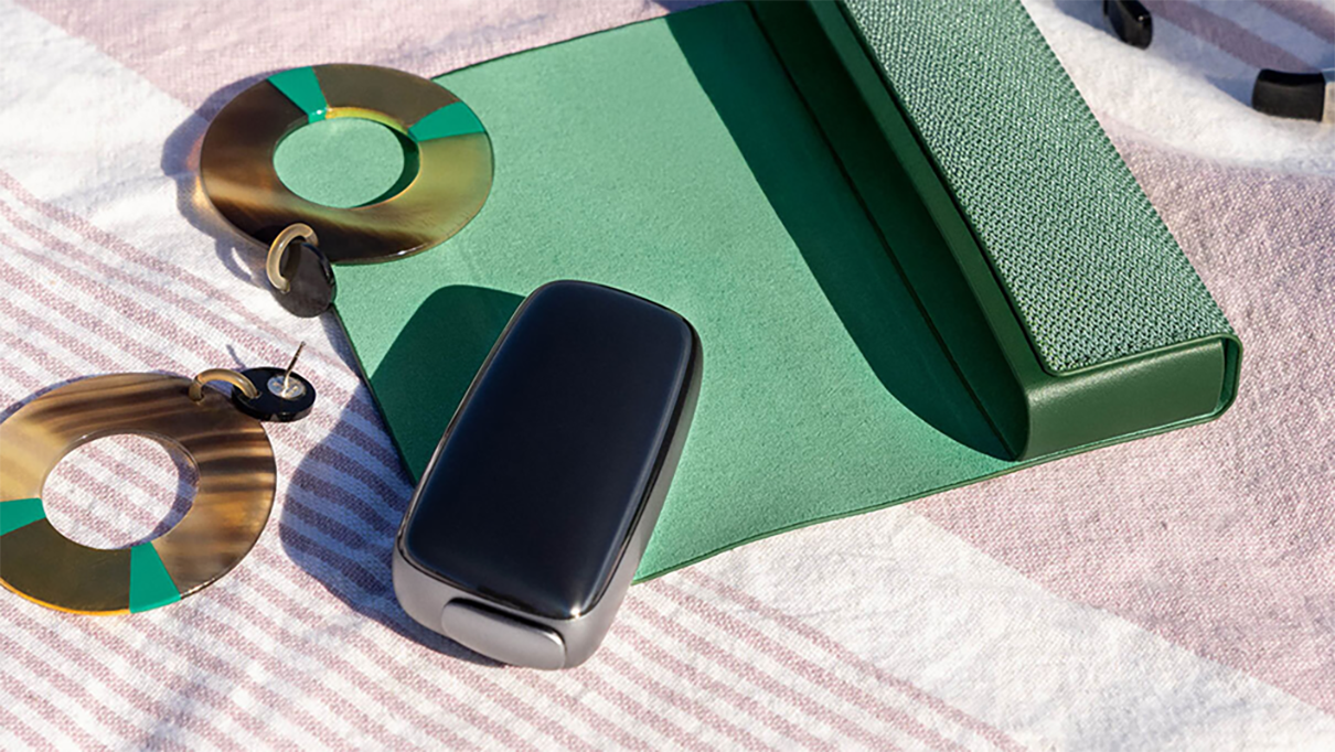Ploom device on a towel next to a green case and modern earrings.   