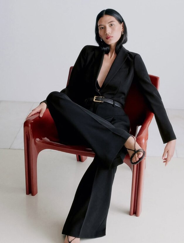 A woman wearing a black, long-sleeved button-up top with slim trousers