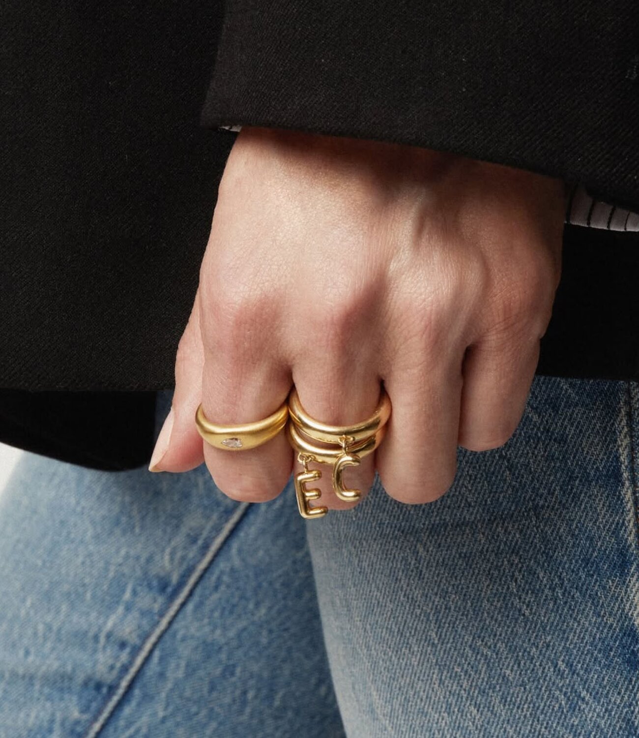 A woman wearing a dark grey herringbone wool blazer with a set of yellow gold, diamond-embellished necklace, rings, ear cuff and bangle