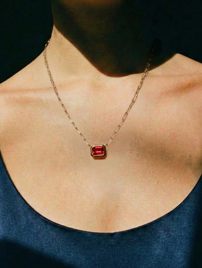 A person wearing a yellow gold chain necklace featuring a rectangular garnet pendant