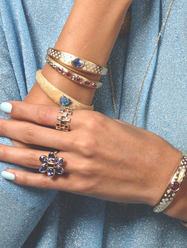 A person wearing multiple gem-embellished yellow gold bangles and rings