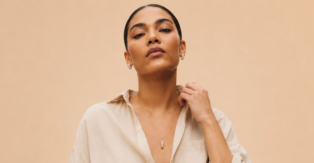 A woman wearing a dark grey herringbone wool blazer with a set of yellow gold, diamond-embellished necklace, rings, ear cuff and bangle