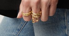 A woman wearing a dark grey herringbone wool blazer with a set of yellow gold, diamond-embellished necklace, rings, ear cuff and bangle