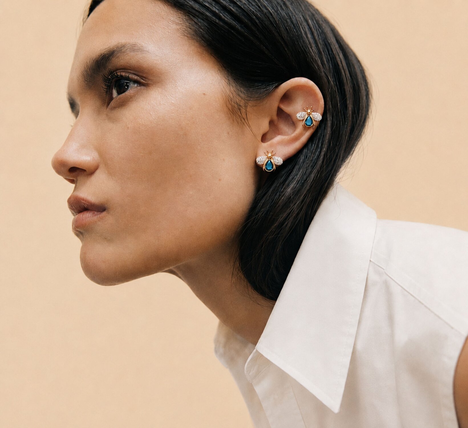 A woman wearing a dark grey herringbone wool blazer with a set of yellow gold, diamond-embellished necklace, rings, ear cuff and bangle