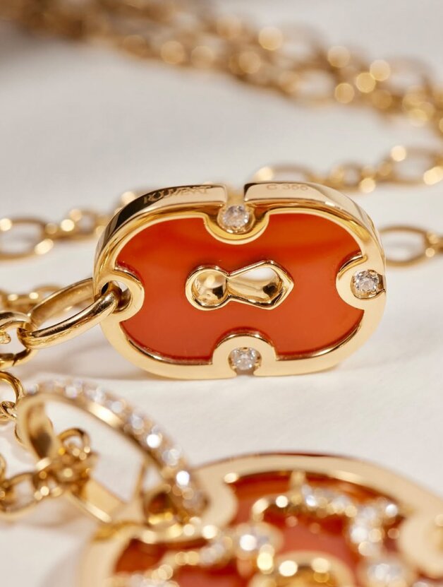 A gold chain necklace featuring an orange enamel inlay with diamonds
