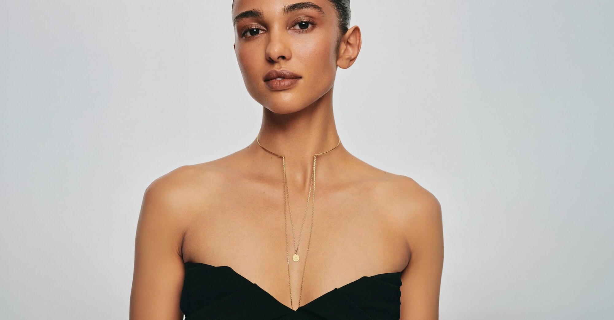A woman wearing a dark grey herringbone wool blazer with a set of yellow gold, diamond-embellished necklace, rings, ear cuff and bangle