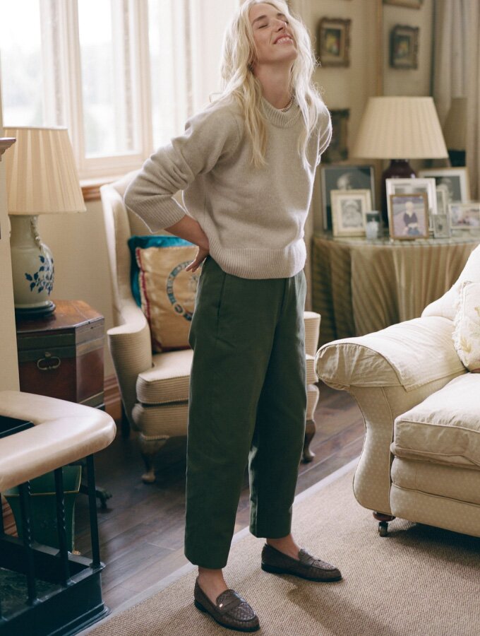 A woman wearing a beige long-sleeved crew neck knit sweater with army green pants and brown loafers