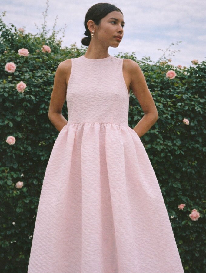 A woman wearing a light pink sleeveless matelassé midi dress