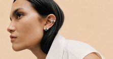 A woman wearing a dark grey herringbone wool blazer with a set of yellow gold, diamond-embellished necklace, rings, ear cuff and bangle