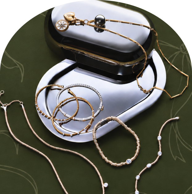 Gold and silver-toned necklaces and bracelets arranged around polished silver trays on patterned olive-green fabric.