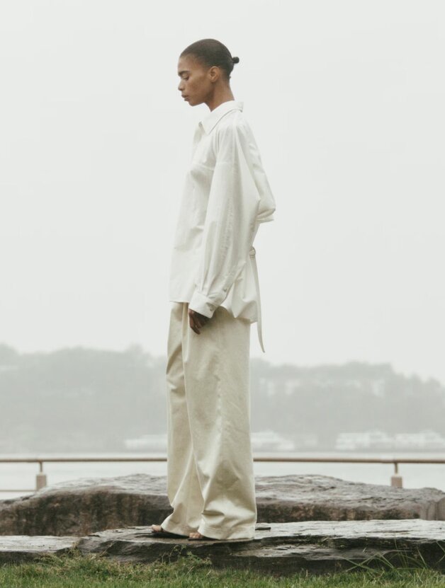 A woman wearing a white draped long-sleeved button-up top with beige pants