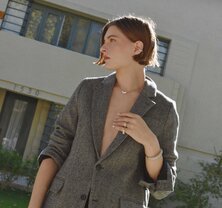 A woman wearing a dark grey herringbone wool blazer with a set of yellow gold, diamond-embellished necklace, rings, ear cuff and bangle