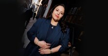 A woman wearing a dark grey herringbone wool blazer with a set of yellow gold, diamond-embellished necklace, rings, ear cuff and bangle