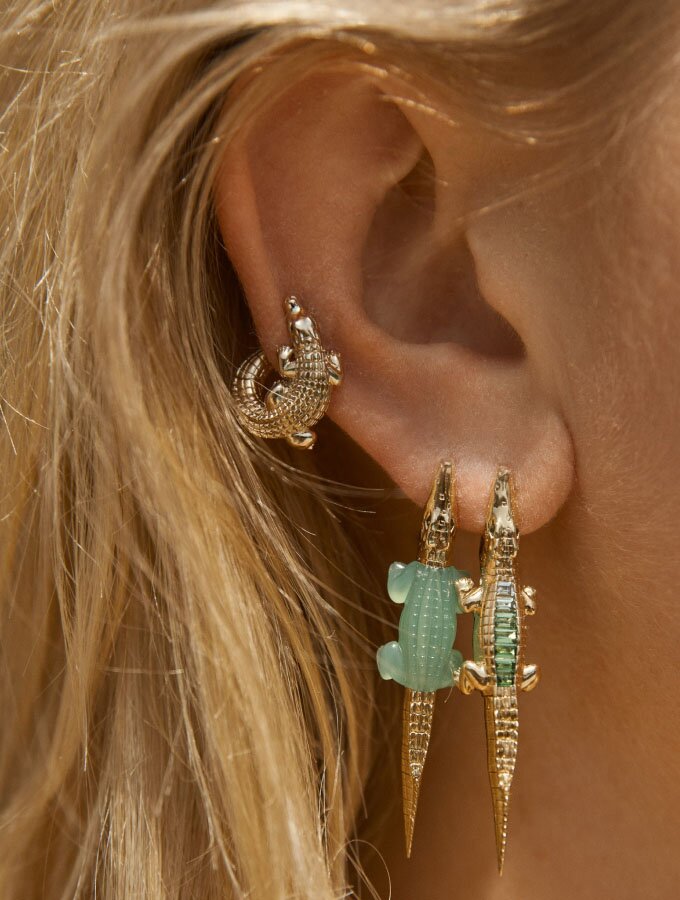 A woman wearing three yellow gold earrings featuring an alligator motif