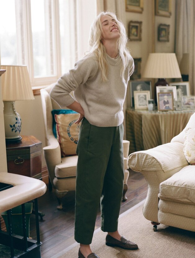 A woman wearing a beige long-sleeved crew neck knit sweater with army green pants and brown loafers