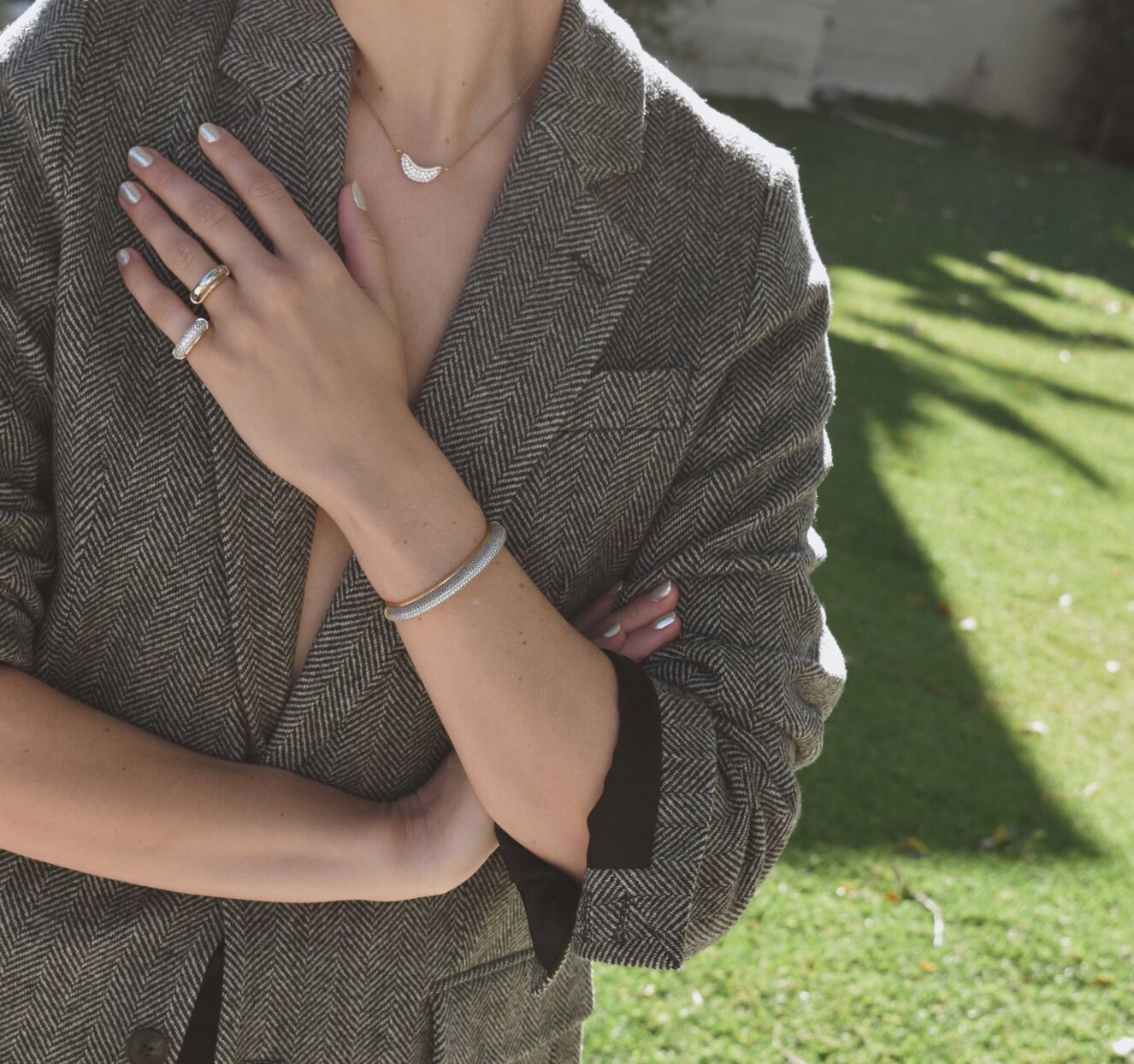 A woman wearing a dark grey herringbone wool blazer with a set of yellow gold, diamond-embellished necklace, rings, ear cuff and bangle