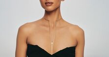 A woman wearing a dark grey herringbone wool blazer with a set of yellow gold, diamond-embellished necklace, rings, ear cuff and bangle