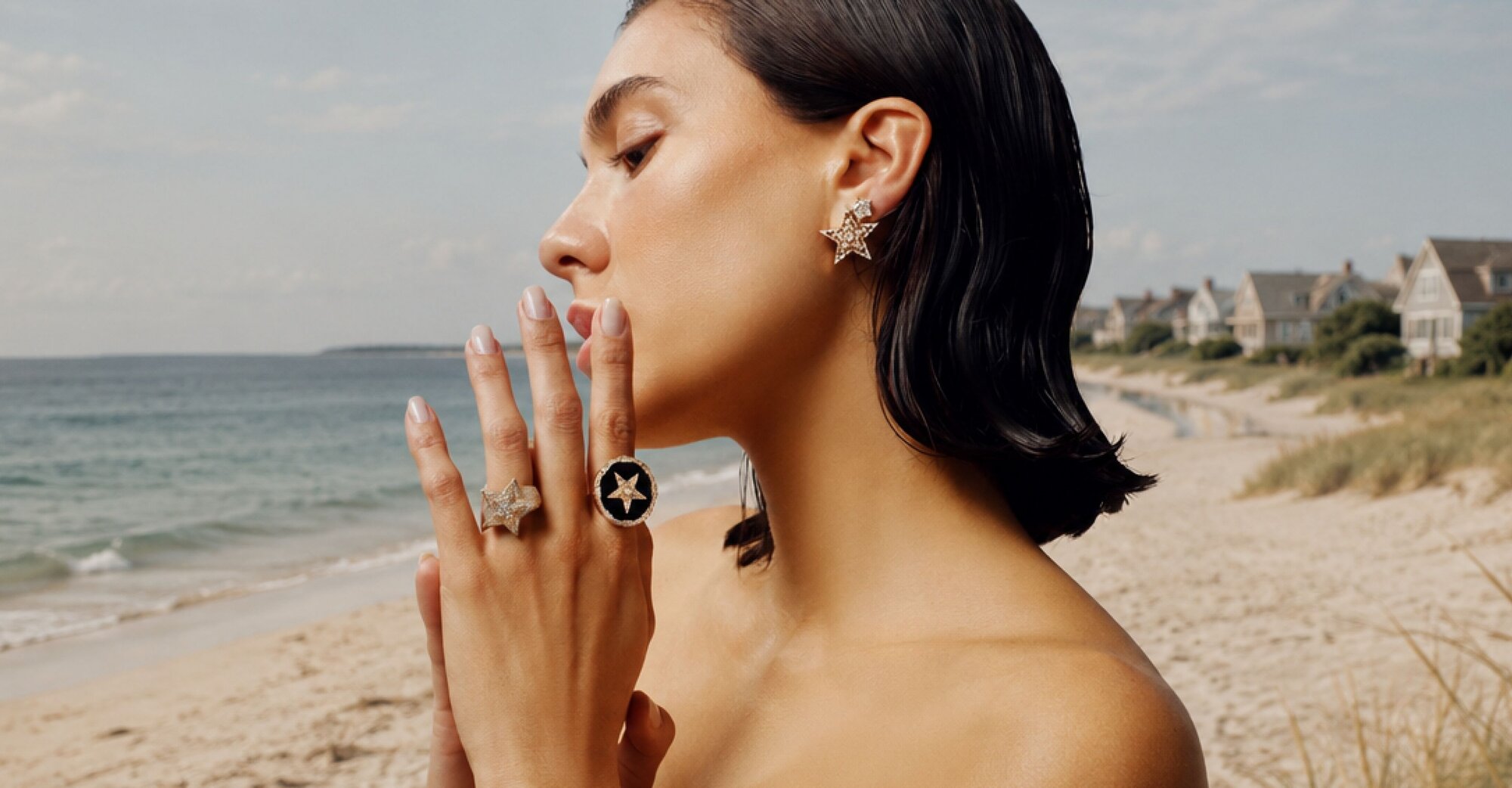 A woman wearing a dark grey herringbone wool blazer with a set of yellow gold, diamond-embellished necklace, rings, ear cuff and bangle