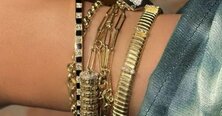 A woman wearing a dark grey herringbone wool blazer with a set of yellow gold, diamond-embellished necklace, rings, ear cuff and bangle