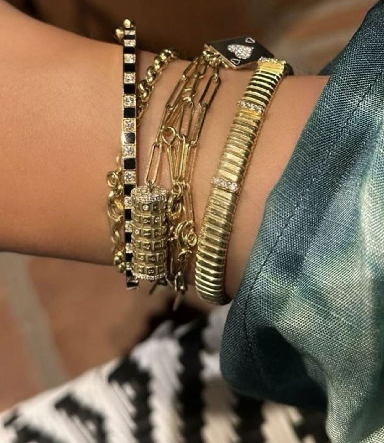 A woman wearing a dark grey herringbone wool blazer with a set of yellow gold, diamond-embellished necklace, rings, ear cuff and bangle